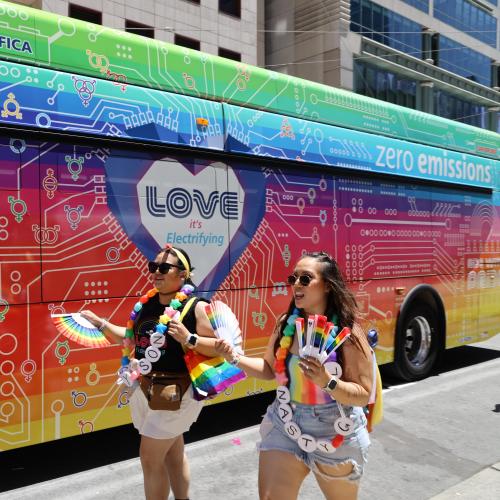 Pride-goers walk next SamTrans bus wrapped for the event