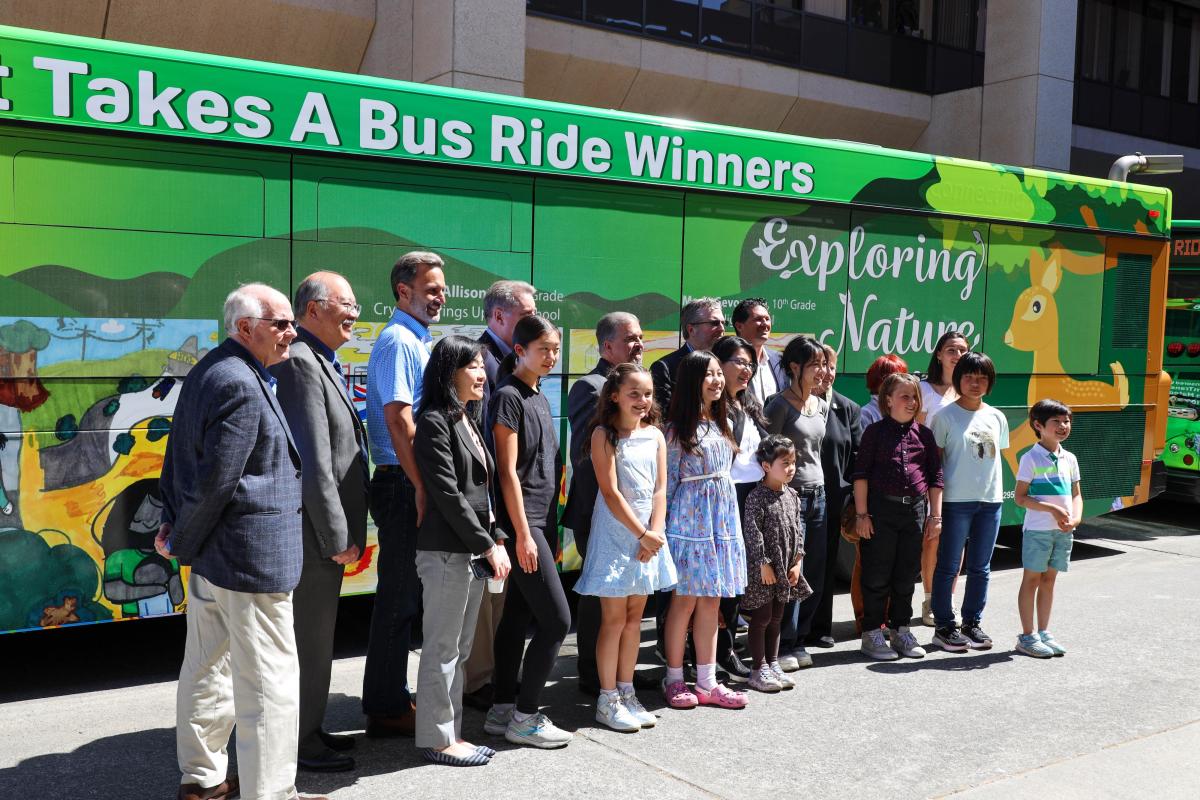 Contest winners gather by Bus wrapped with their artwork